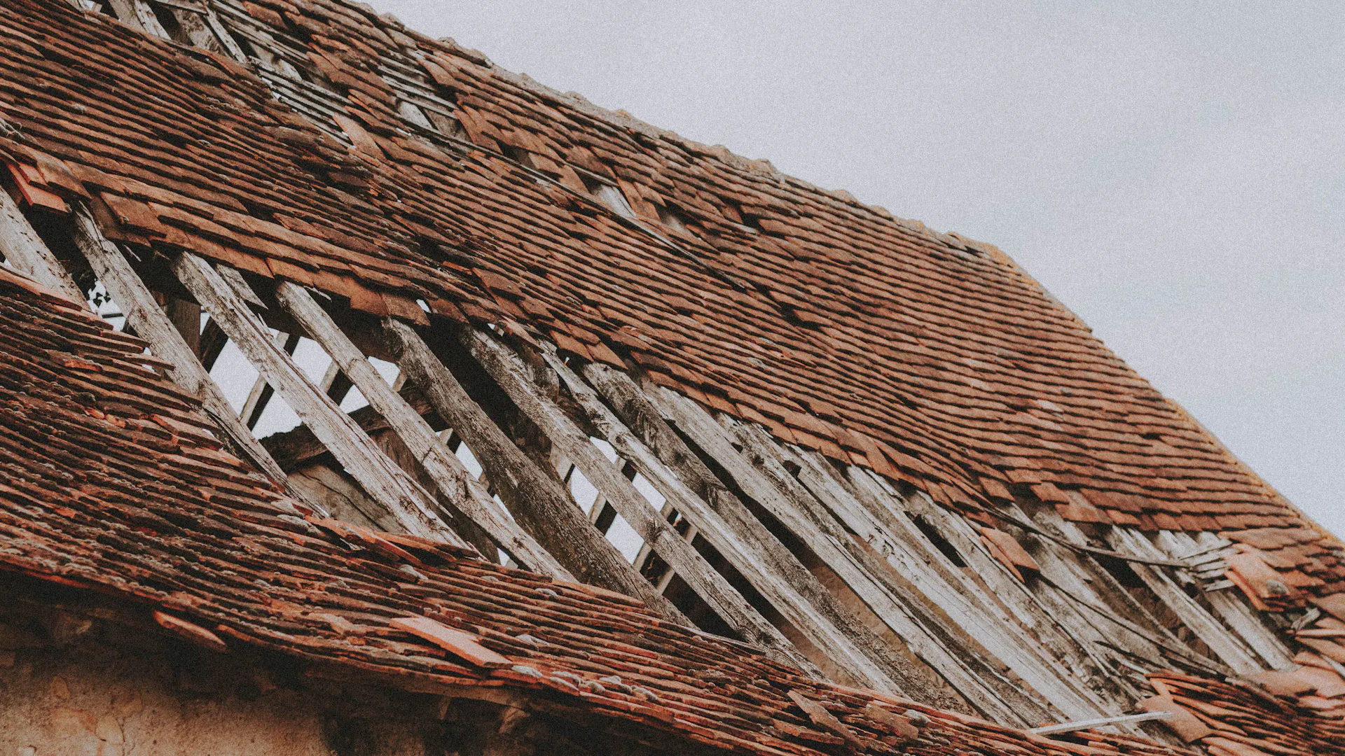 Close-up of a dilapidated roof with missing shingles and exposed wooden framing after storm and wind damage